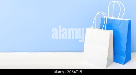 Weiße blaue Handarbeitspapiertaschen. Shopping Mockup Taschen Papier-Pakete auf weißem Tisch blaues Licht Hintergrund mit Kopierraum. Einkaufen, Verkauf, Lieferung von Lebensmitteln Stockfoto