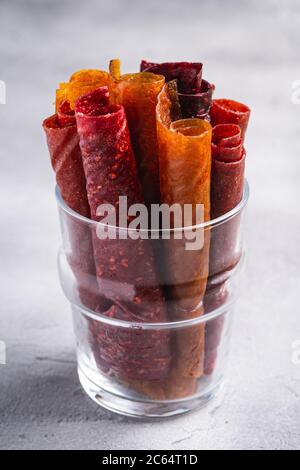 Obstpastilien in Glas Tasse auf Stein Beton Hintergrund. Bio-zuckerfreies Roll-up-Lebensmittel aus Himbeere, Erdbeere, Pfirsich und Apfel. Veganes Zuhause Stockfoto