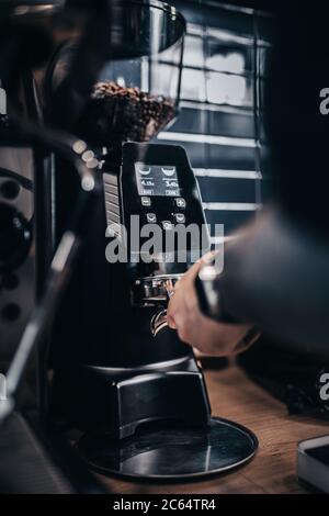 Der Barista nimmt gemahlenen Kaffee von einer Kaffeemühle in einen Halter und macht Espresso in einem Café Stockfoto