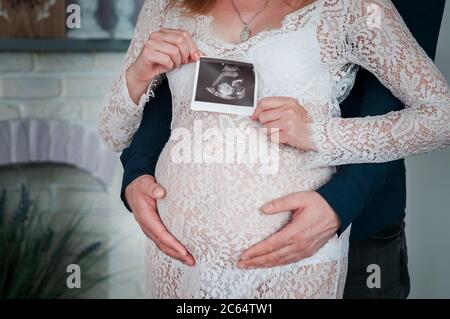 Mann und Frau halten eine Momentaufnahme eines Ultraschalls auf einem schwangeren Bauch Stockfoto