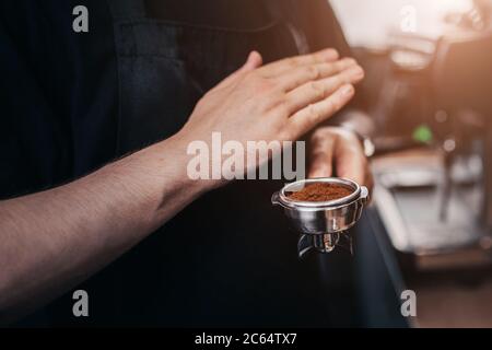 Der Barista Professional schüttelt und kondensiert gemahlenen Kaffee im Halter mit scharfen kurzen Handbewegungen Stockfoto