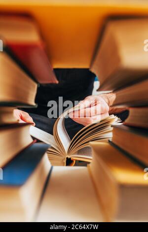 Durch das Loch zwischen den Büchern auf einem Regal in der Bibliothek können Sie die Hände einer Person sehen - Blättern durch die Seiten Stockfoto