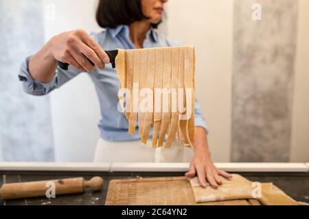 Frau, die in einer Küche steht und frische hausgemachte Tagliatelle-Pasta zubereitet. Stockfoto