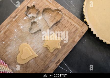 Nahaufnahme von Ausstechformen mit hohem Winkel und Ausschneiden von Teig in Stern- und Herzform auf Holzschneidebrett. Stockfoto