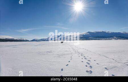 Blick über den gefrorenen See mit Menschen in der Ferne, drei Fußspuren Stockfoto