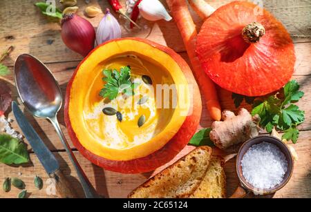 Kürbissuppe in einem Kürbis auf rustikalem Holztisch serviert Stockfoto