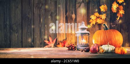 Thanksgiving Hintergrund mit Kürbissen, Laterne, Früchten und fallenden Blättern auf rustikalem Holztisch Stockfoto