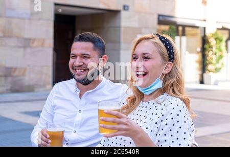 Multiethnisches Paar lächelt, lacht und plaudert mit Freunden an der Bar, trinkt Bier und feiert das Ende der Sperre, trägt Masken unter Stockfoto