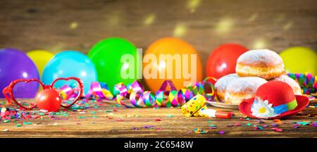 Krapfen, berliner oder Donuts mit Fliege, Partyhut, Luftschlangen, Konfetti und Luftballons. Bunte Party, Karneval oder Geburtstag Hintergrund Stockfoto