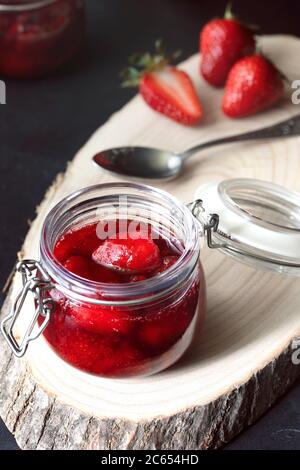 Glas mit hausgemachter Erdbeermarmelade mit reifen Erdbeeren und Löffeln auf einem Holztablett Stockfoto