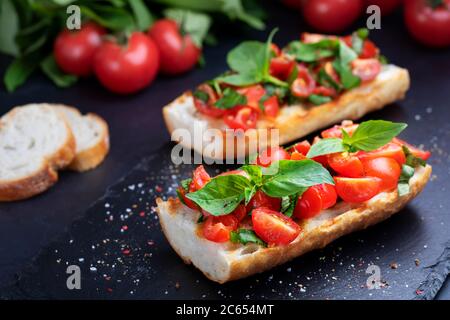 Hausgemachte Bruschetta mit Kirschtomaten und Basilikum auf einem Schieferbrett. Italienische Küche. Antipasti. Vegane Küche Stockfoto