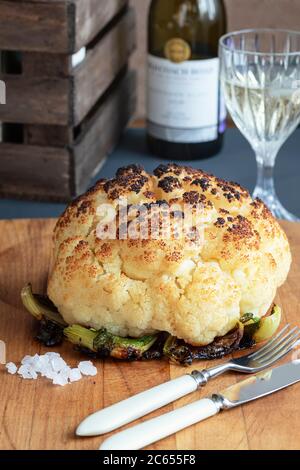 Ganze gegrillte Blumenkohl aus dem Ofen mit Meersalz und Weißwein auf einem Holzbrett. Vegane Küche. Vegetarische Gerichte. Kochen zu Hause Stockfoto