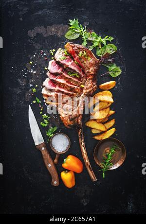 Gegrilltes Fleisch, ​​tomahawk Rindersteak mit Gewürzen, pommes frites und Gemüse auf rustikalem Hintergrund Stockfoto