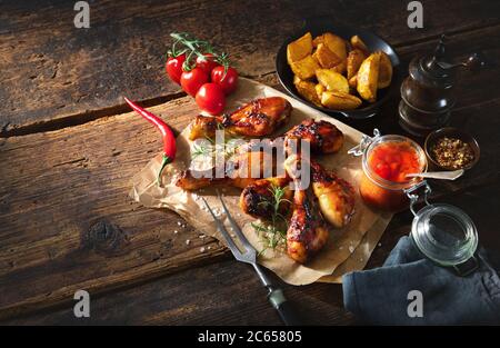 Gegrillter Hähnchendrumstick auf Papier mit pommes Frites und Sauce, Nahaufnahme auf rustikalem Holztisch Stockfoto