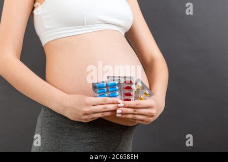 Zugeschnittenes Bild von Medikamenten in Blasen in den Händen der schwangeren Frau auf buntem Hintergrund mit Kopierfläche. Einnahme von Vitamin-Pillen während der Schwangerschaft conce Stockfoto