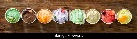 Verschiedene bunte Eiscreme-Sorten mit Früchten in Pappbechern auf rustikalem Holzhintergrund Stockfoto