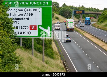 East Lothian, Schottland, Großbritannien, 7. Juli 2020. Covid-19 neue Meldung auf A1-Gantry: Die dritte Version der Pandemie-Meldung erscheint auf der über-Gantry in der Nähe von Haddington, die lautet "Lokale Reisebeschränkungen sicher bleiben", da Schottland in Phase 3, die nächste Woche erwartet wird, eingeht. Der Verkehr auf der zweispurigen Fahrbahn ist viel schwerer als in den letzten Monaten zu sehen war Stockfoto