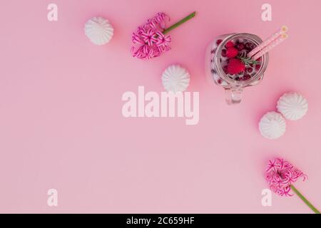 Beeren-Smoothie mit Strohhalmen, Marshmallow und Blumen auf rosa Hintergrund. Flach liegend. Draufsicht Stockfoto