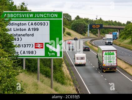 East Lothian, Schottland, Großbritannien, 7. Juli 2020. Covid-19 neue Meldung auf A1-Gantry: Die dritte Version der Pandemie-Meldung erscheint auf der über-Gantry in der Nähe von Haddington, die lautet "Lokale Reisebeschränkungen sicher bleiben", da Schottland in Phase 3, die nächste Woche erwartet wird, eingeht. Der Verkehr auf der zweispurigen Fahrbahn ist viel schwerer als in den letzten Monaten zu sehen war Stockfoto