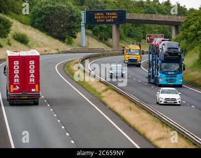 East Lothian, Schottland, Großbritannien, 7. Juli 2020. Covid-19 neue Meldung auf A1-Gantry: Die dritte Version der Pandemie-Meldung erscheint auf der über-Gantry in der Nähe von Haddington, die lautet "Lokale Reisebeschränkungen sicher bleiben", da Schottland in Phase 3, die nächste Woche erwartet wird, eingeht. Der Verkehr auf der zweispurigen Fahrbahn ist viel schwerer als in den letzten Monaten zu sehen war Stockfoto