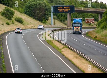 East Lothian, Schottland, Großbritannien, 7. Juli 2020. Covid-19 neue Meldung auf A1-Gantry: Die dritte Version der Pandemie-Meldung erscheint auf der über-Gantry in der Nähe von Haddington, die lautet "Lokale Reisebeschränkungen sicher bleiben", da Schottland in Phase 3, die nächste Woche erwartet wird, eingeht. Der Verkehr auf der zweispurigen Fahrbahn ist viel schwerer als in den letzten Monaten zu sehen war Stockfoto