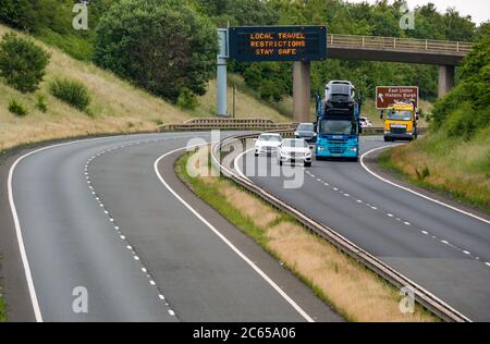 East Lothian, Schottland, Großbritannien, 7. Juli 2020. Covid-19 neue Meldung auf A1-Gantry: Die dritte Version der Pandemie-Meldung erscheint auf der über-Gantry in der Nähe von Haddington, die lautet "Lokale Reisebeschränkungen sicher bleiben", da Schottland in Phase 3, die nächste Woche erwartet wird, eingeht. Der Verkehr auf der zweispurigen Fahrbahn ist viel schwerer als in den letzten Monaten zu sehen war Stockfoto