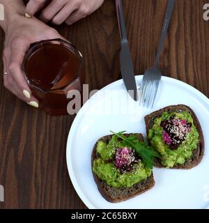 Pürierte Avocado-Toasts auf Vollkornbrot mit einem Glas Eiskaffee. Vegetarisch. Konzept für das ganze Essen. Stockfoto