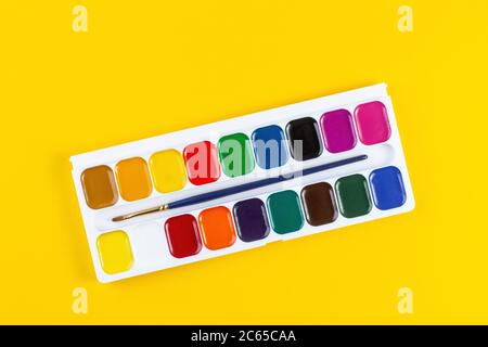 Draufsicht der Aquarellfarben mit Pinsel in Box auf gelbem Hintergrund. Flach liegend mit Kopierplatz Stockfoto
