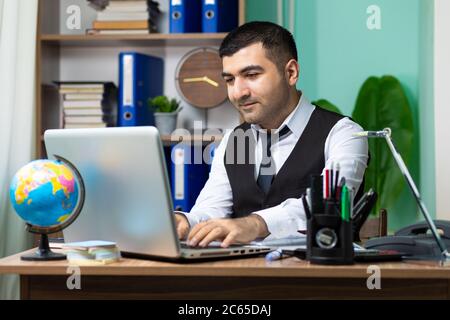 Junger Geschäftsmann, der am Tisch im Büro am Laptop arbeitet Stockfoto