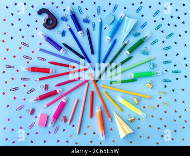 Zurück in die Schule mit verschiedenen Schulbedarf und sternförmigen Konfetti in Regenbogenfarben auf pastellblauem Hintergrund. Flach liegend. Stockfoto
