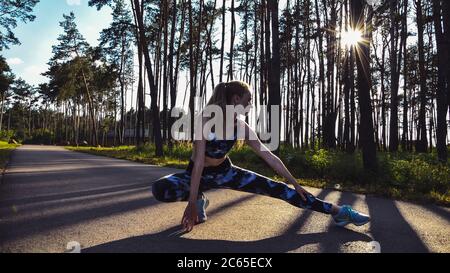 Frau macht Yoga im Wald gegen Himmel und Sonne. Hartes Licht. Silhouette des Mädchens tun Outdoor Sport Stretch. Stockfoto