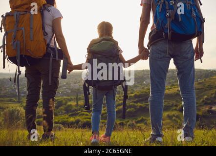 Glückliche Familie mit Rucksäcken auf die Natur bei Sonnenuntergang. Wandern Familien Tourismus Konzept. Rückansicht. Stockfoto