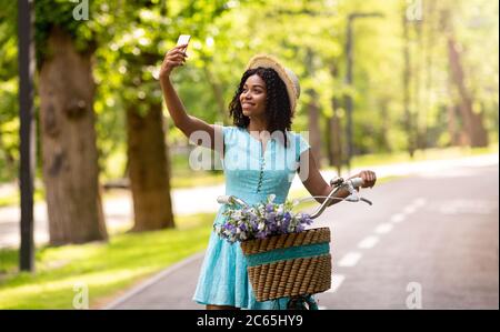 Ziemlich schwarzes Mädchen mit Fahrrad Selfie auf dem Smartphone in schönen Sommerpark Stockfoto