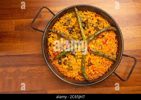Gemüsepaella Reis mit Gemüse in Paella Pfanne, auf Holzboden. Stockfoto