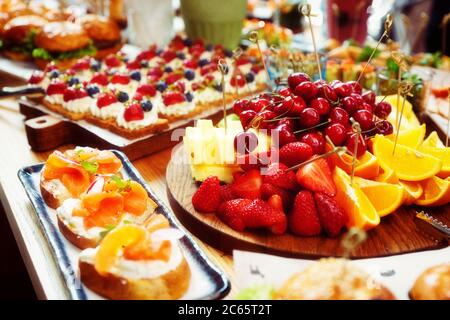 Obst, Beeren, Fisch-Snacks und Dessert auf Catering-Restaurant-Tisch, getönte Stockfoto