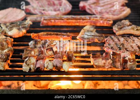 Eine Auswahl an frischem Fleisch Grillen auf einem BBQ-Feuer in der Nähe auf dem Grill und heiße Kohlen mit Fokus auf Rindfleisch Kebabs oder Spieße in der Mitte Stockfoto
