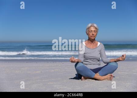 Ältere kaukasische Frau meditiert am Strand. Stockfoto