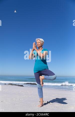 Ältere kaukasische Frau sitzt auf Sand und praktiziert Yoga Stockfoto