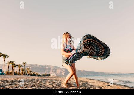 Frau läuft und hält Schal auf Welle entspannen und glücklich am Strand Stockfoto