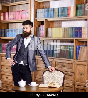 Bücher, Erfolg, Retro, Vintage-Konzept. Regisseur mit langen Bartständern im luxuriösen Interieur. Bärtiger Mann in elegantem Anzug lächelt. Reifer Mann in der Nähe Bücherregal und Tisch mit Teekanne. Mode und Style. Stockfoto