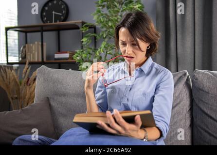 Schöne Frau, die bequem auf dem Sofa sitzt und Buch liest Stockfoto