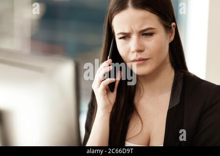 Krisenkonzept. Junge Geschäftsfrau am Bürotisch sitzen beschäftigt reden auf einem Handy Lösung eines sehr ernsten Arbeitsproblem. Frau in Stockfoto