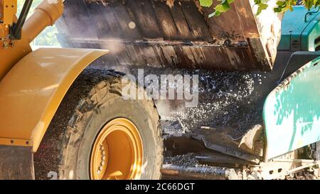 Schaufeltraktor gießt heißen Asphalt in einen Grader, Bau einer neuen Straße in einer Stadt, Material für Straßenbau Nahaufnahme. Stockfoto