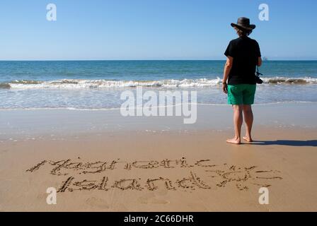 Frau, die am Strand steht und eine Kamera mit Blick aufs Meer hält, mit den Worten Magnetic Island im nassen Sand. Queensland, Australien Stockfoto