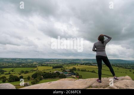 Eine schwarze Frau, die auf einem Felsen steht und den wolkigen Horizont in sportlicher Kleidung betrachtet Stockfoto