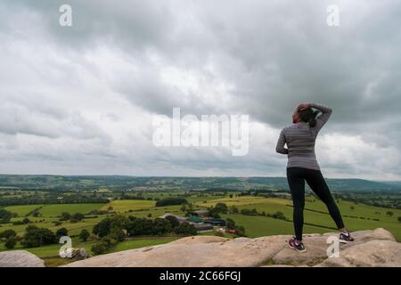 Eine schwarze Frau, die auf einem Felsen steht und den wolkigen Horizont in sportlicher Kleidung betrachtet Stockfoto