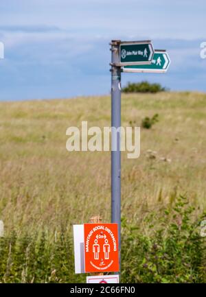 East Lothian, Schottland, Großbritannien, 7. Juli 2020. UK Wetter: Sonnenschein in Yellowcraig jetzt, da die East Lothian council Parkhäuser eröffnet haben. Es gibt soziale Distanzierungsmaßnahmen, um separate Wege zum und vom Strand zu schaffen. Ein physikalisches Distanzierungszeichen auf dem John Muir Weg Stockfoto