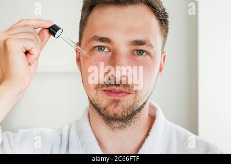Junger Mann, der Serum oder andere Hautpflegeprodukte auf sein Gesicht auftragen wird. Stockfoto