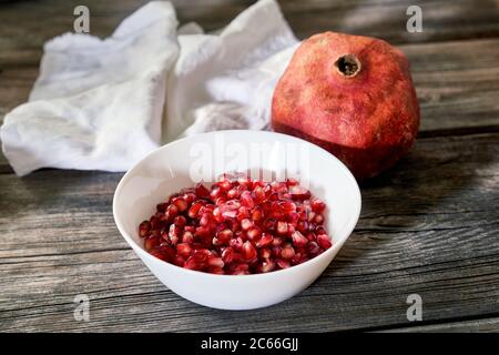 Granatapfelkerne in weißer Schale und ein ganzer Granatapfel auf einem Holztisch Stockfoto