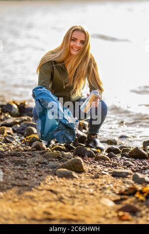 Junge Frau Freiwillige Abholung Aerosoldose am Strand Stockfoto